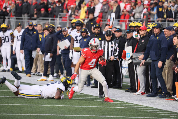 College Football: Ohio State Julian Fleming (4) in action, runs with the football vs Michigan at Ohio Stadium. Football analyst Connor Stalions and head coach Jim Harbaugh present in the background.
